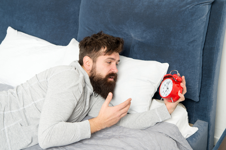 Man With Thick Beard Looking At an Alarm Clock