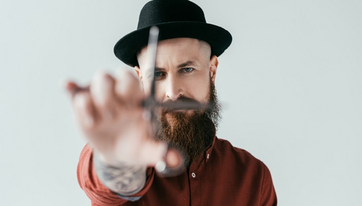 Tattooed and Bearded Barber With a Hat Holding Scissors