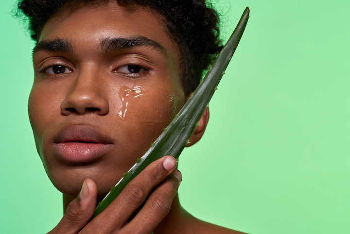 Young Black Guy Touching His Face With Aloe Vera Leaf