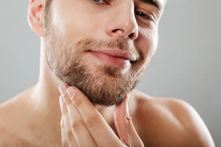 Smiling Young Man With Stubble Beard Touching His Chin