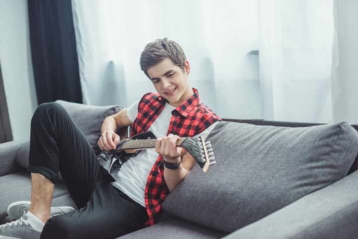 Teenager Playing a Guitar on the Couch