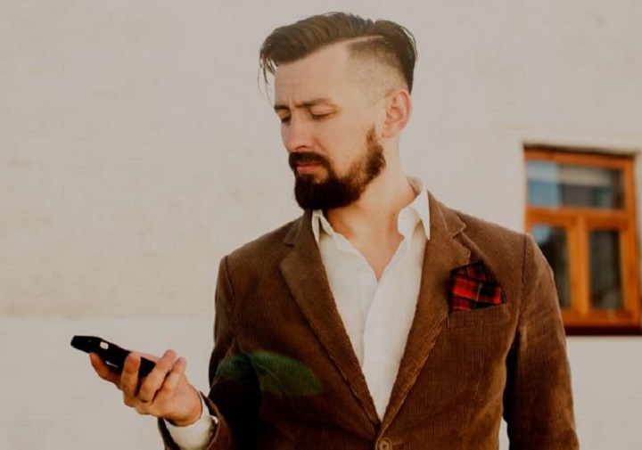 Bearded Man With a Hard Part Haircut Looking at His Phone