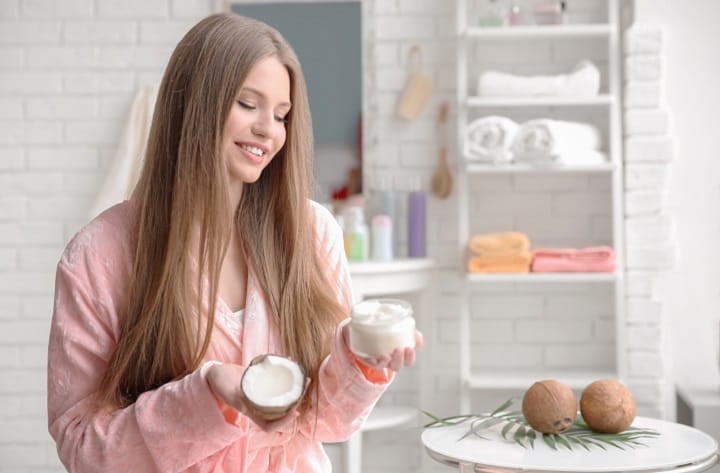 Smiling Girl With a Long Hait Holding a Tube of Coconut Oil For Hair