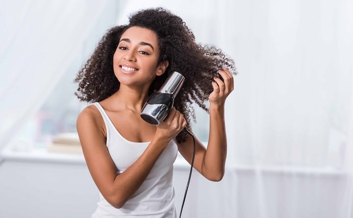 Smiling Woman of COlor Drying Her Curly Hair With a Hair Dryer