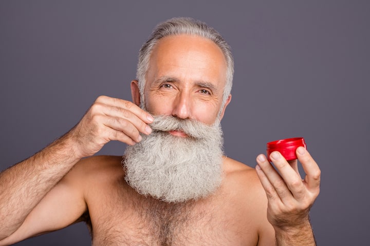 Older Gentleman With Thick Grey Beard Applying Pomade